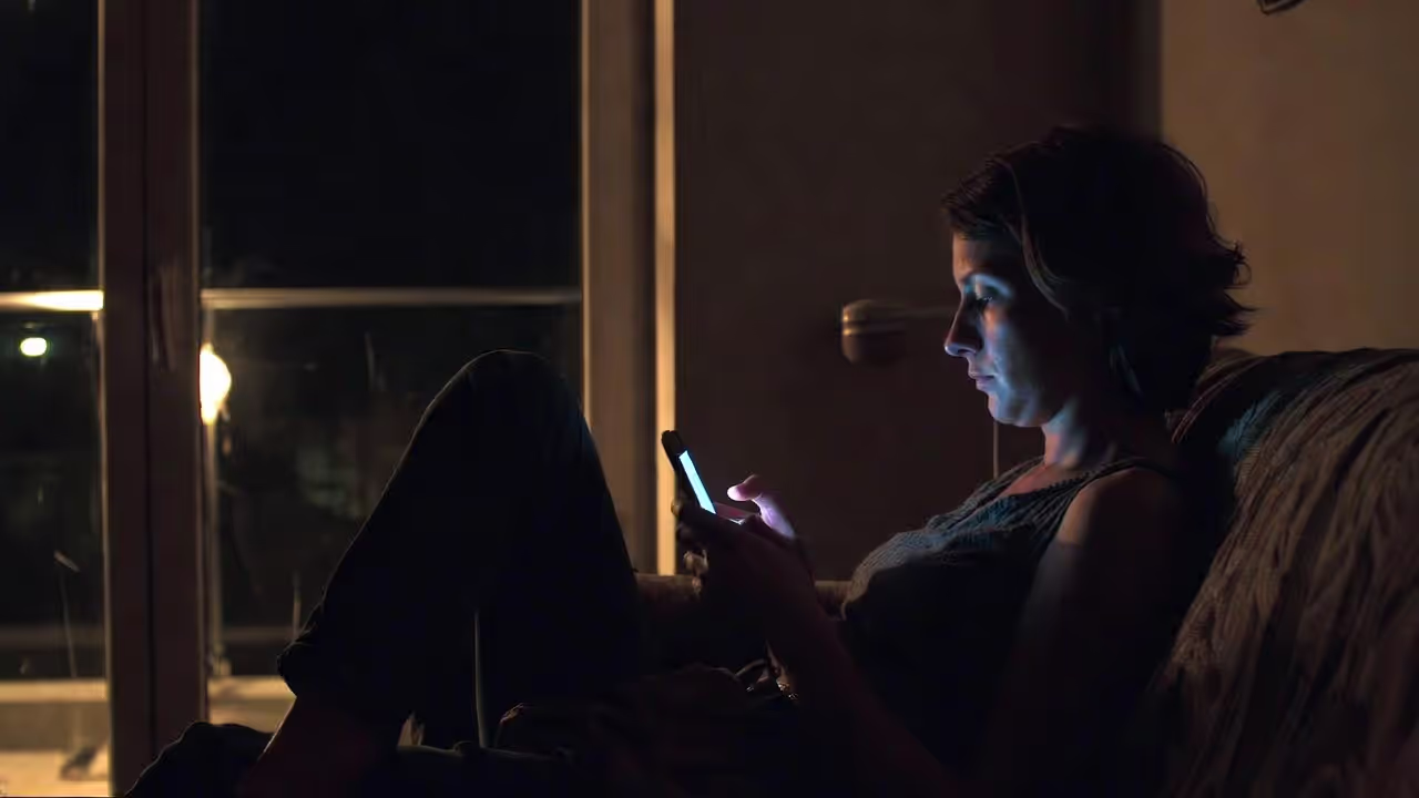 Adult sitting alone at night scrolling on a phone